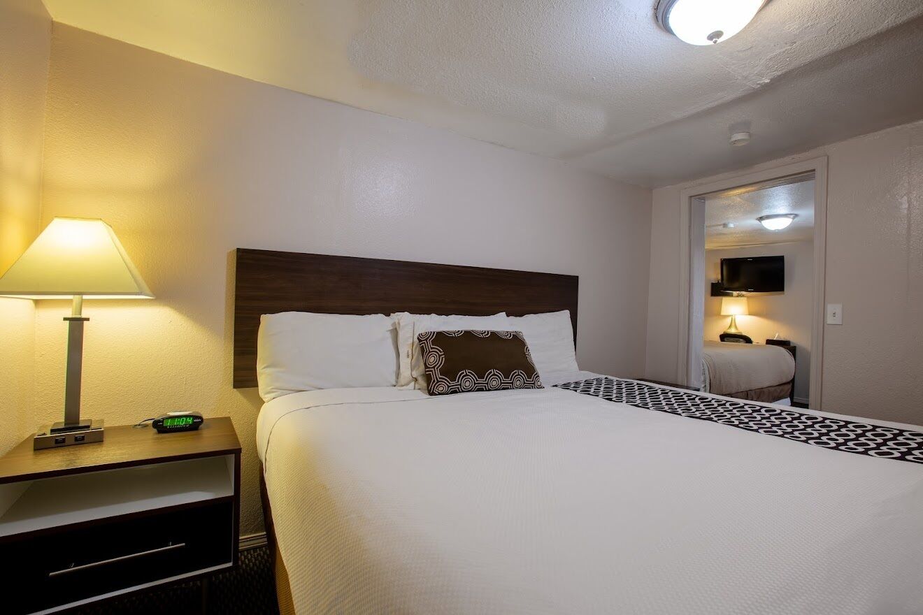 A hotel room with a bed, a nightstand with a lamp, and a television in the corner.
