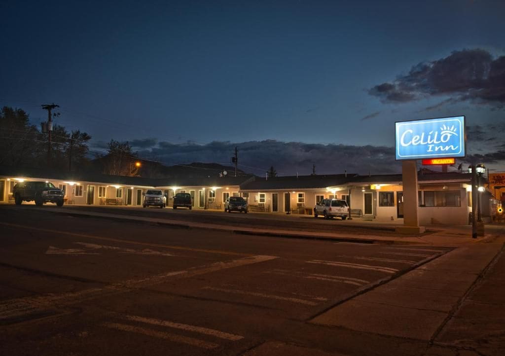 A motel with a neon sign, multiple rooms, and a parking lot at dusk.