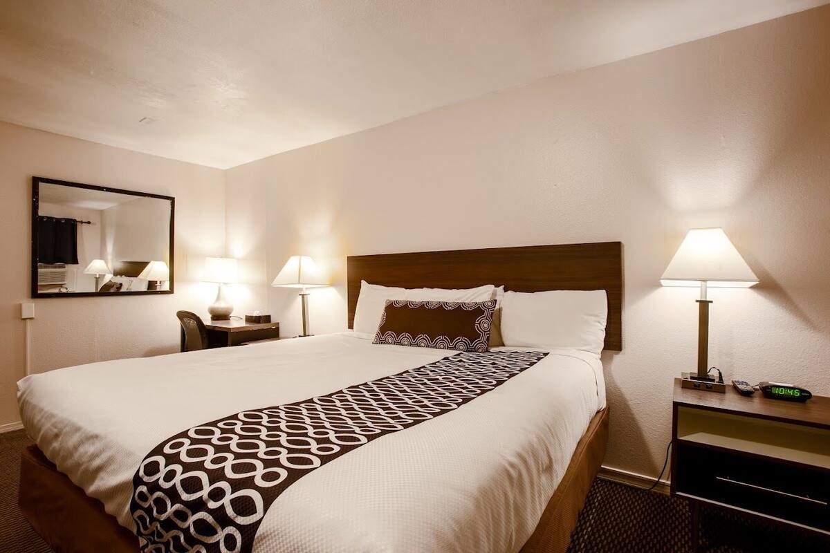 Ein Hotelzimmer mit einem großen Bett, zwei Nachttischen mit Lampen, einem Spiegel und einer Uhr.