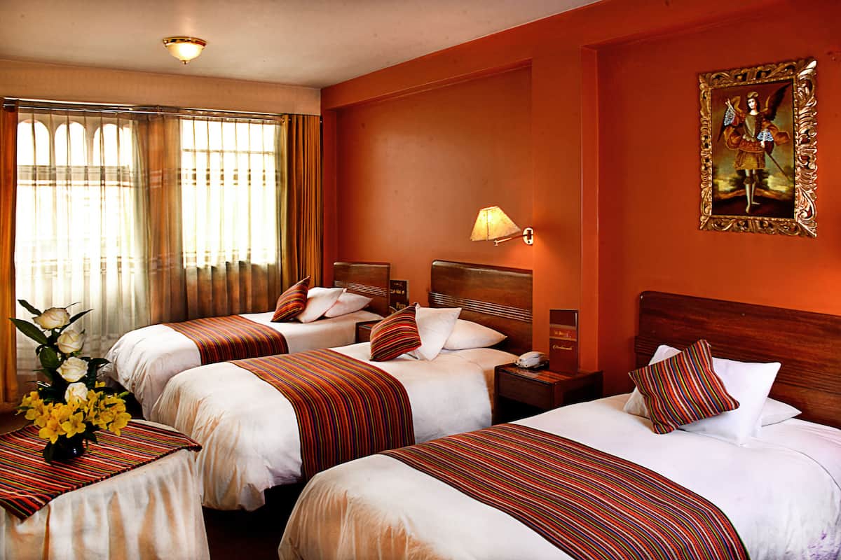 A hotel room with three beds, each with a striped bedspread, a nightstand, a lamp, and a framed picture on the wall.
