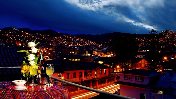 A table with a vase of flowers and two glasses of wine, overlooking a cityscape at night. - Imperial Cusco Hotel (Cusco)