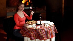 A woman seated at a table with a pizza, wine glass, and plates. - Imperial Cusco Hotel (Cusco)