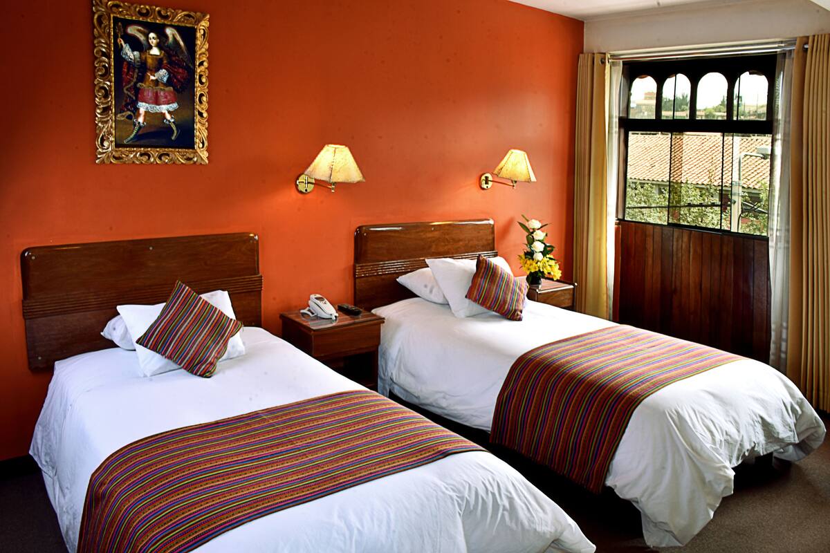 A hotel room with two beds, a wooden headboard, a nightstand with a phone, and a window with curtains.