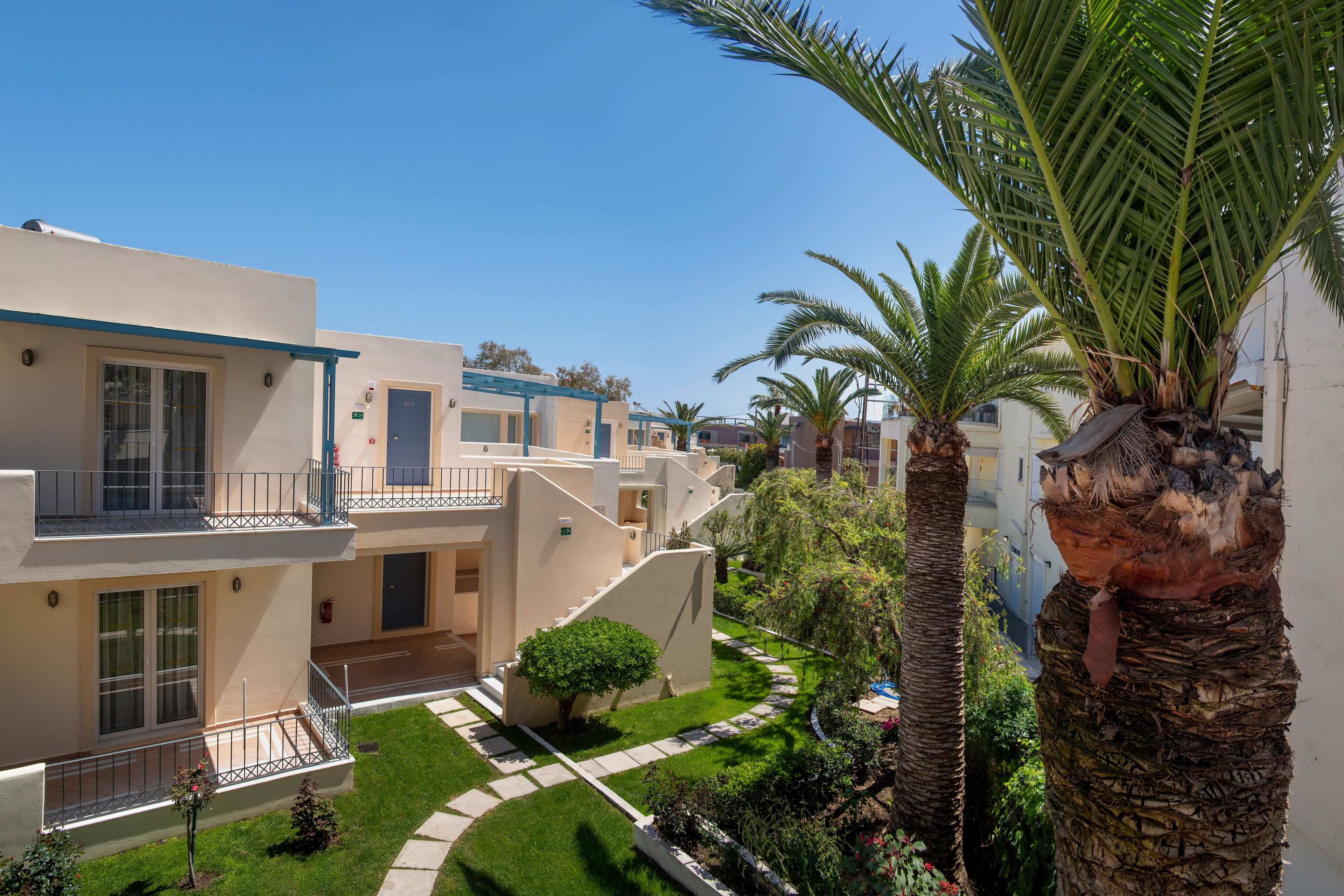 Un edificio residencial con varios balcones, un jardín cuidado y palmeras.