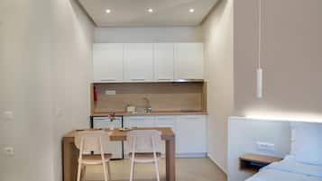 A compact hotel room with a kitchenette, a dining area with two chairs, a bed, and a bedside table.