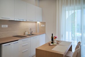 Una cocina moderna con armarios blancos, encimera de madera, lavavajillas integrado y una ventana con cortinas de gasa.