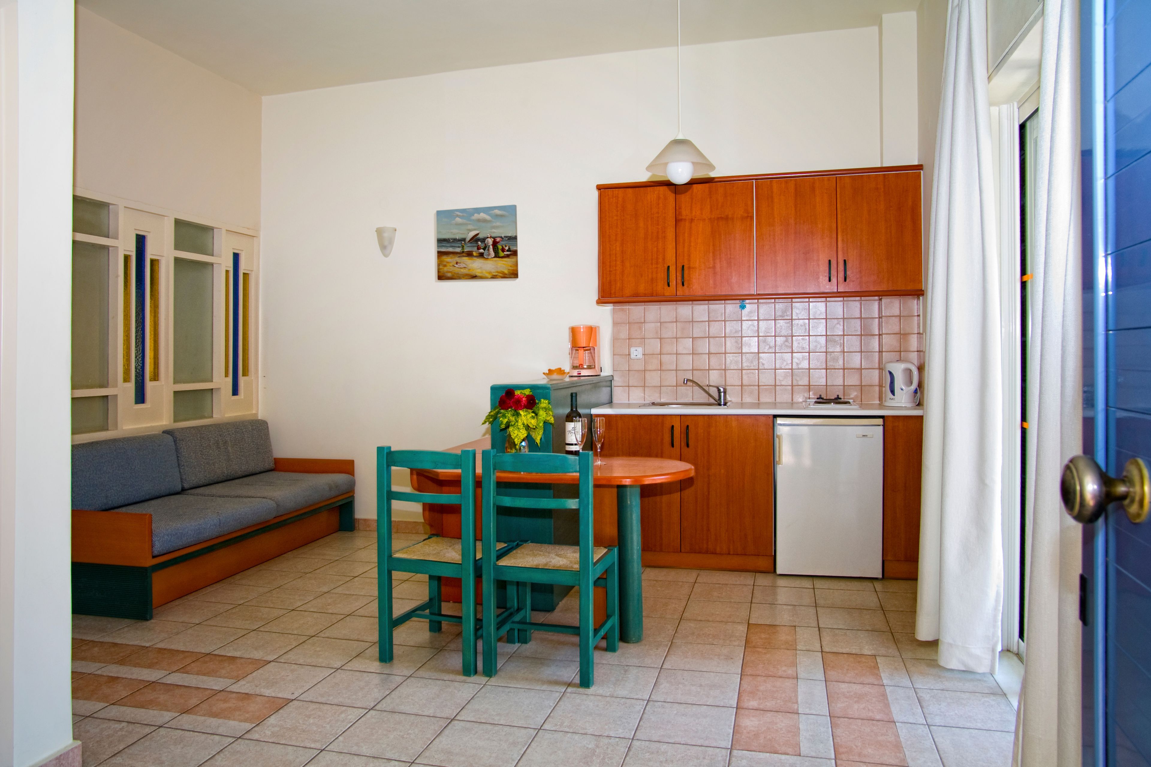 A compact living space with a kitchenette, a dining area with a table and chairs, a sofa, and a painting on the wall.