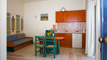 A compact living space with a kitchenette, a dining area with a table and chairs, a sofa, and a painting on the wall.
