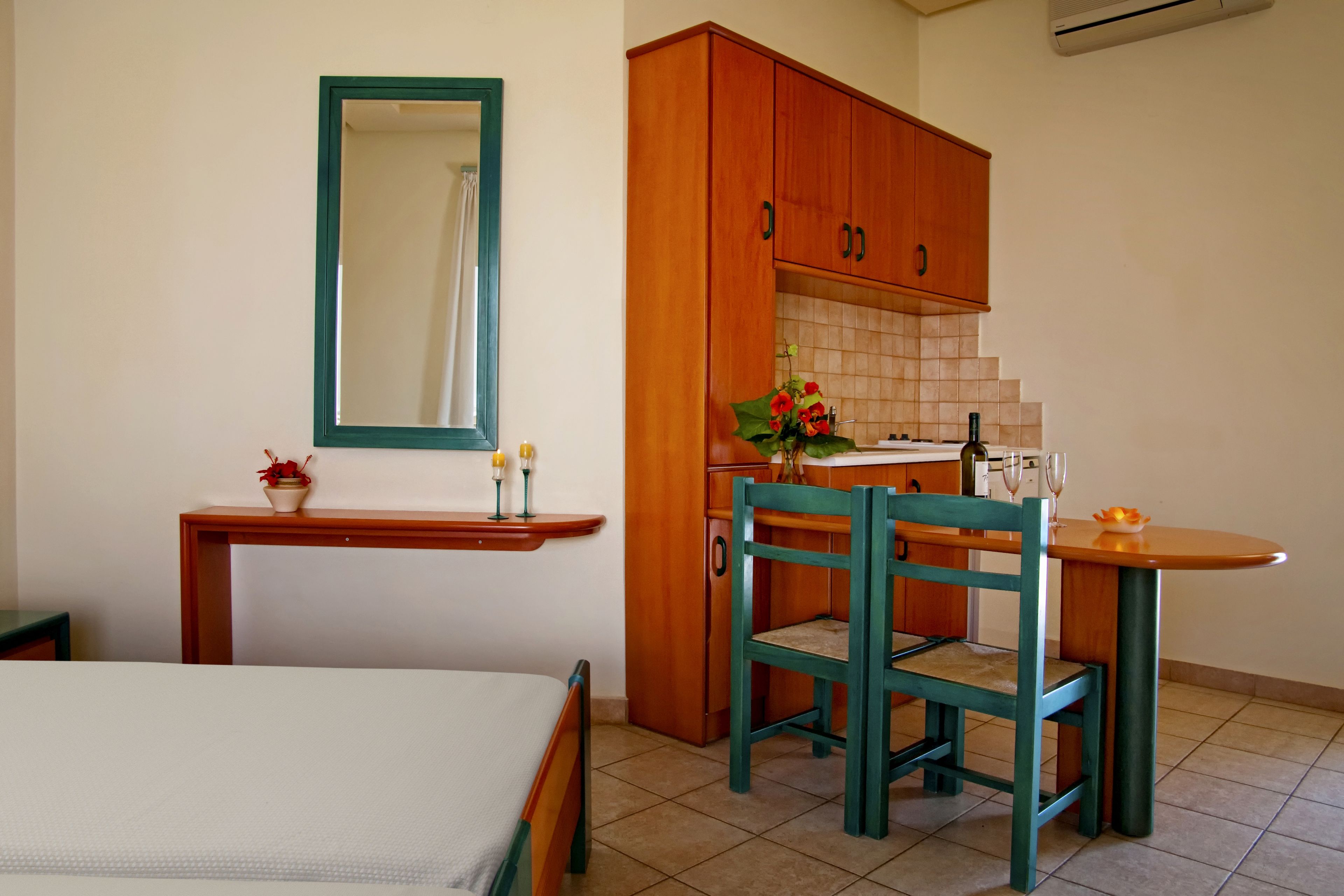 Una habitación pequeña y limpia con una cama, un escritorio de madera, una silla y un espejo.
