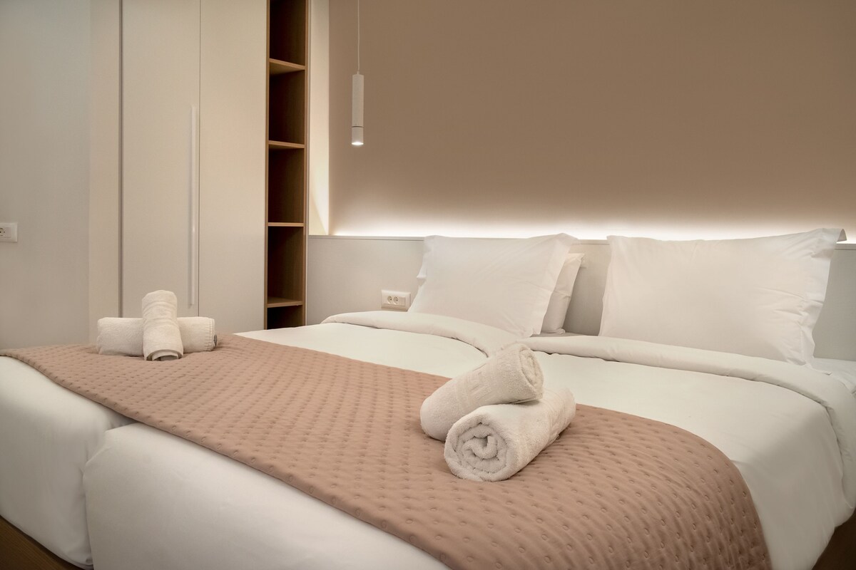 Une chambre d’hôtel moderne avec un lit bien fait, une grande fenêtre et une armoire intégrée.
