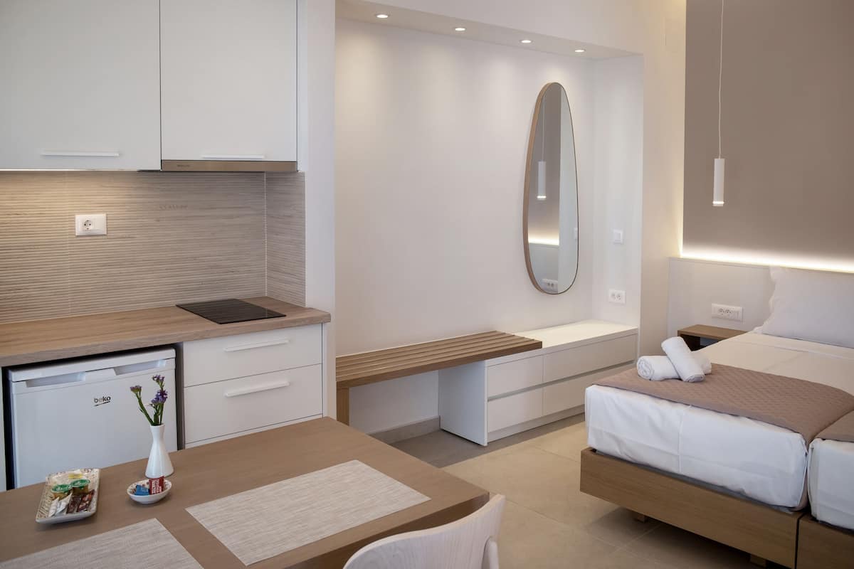 Une chambre d’hôtel moderne équipée d’une kitchenette, d’un lit avec une tête de lit, d’une table de chevet et d’un miroir.