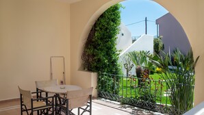Ein Balkon mit Tisch und Stühlen, Blick auf einen Garten und eine weiße Wand mit Grünpflanzen.