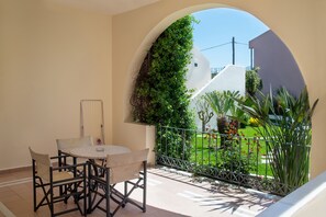 Un balcón con mesa y sillas, vista a un jardín y una pared blanca con plantas.