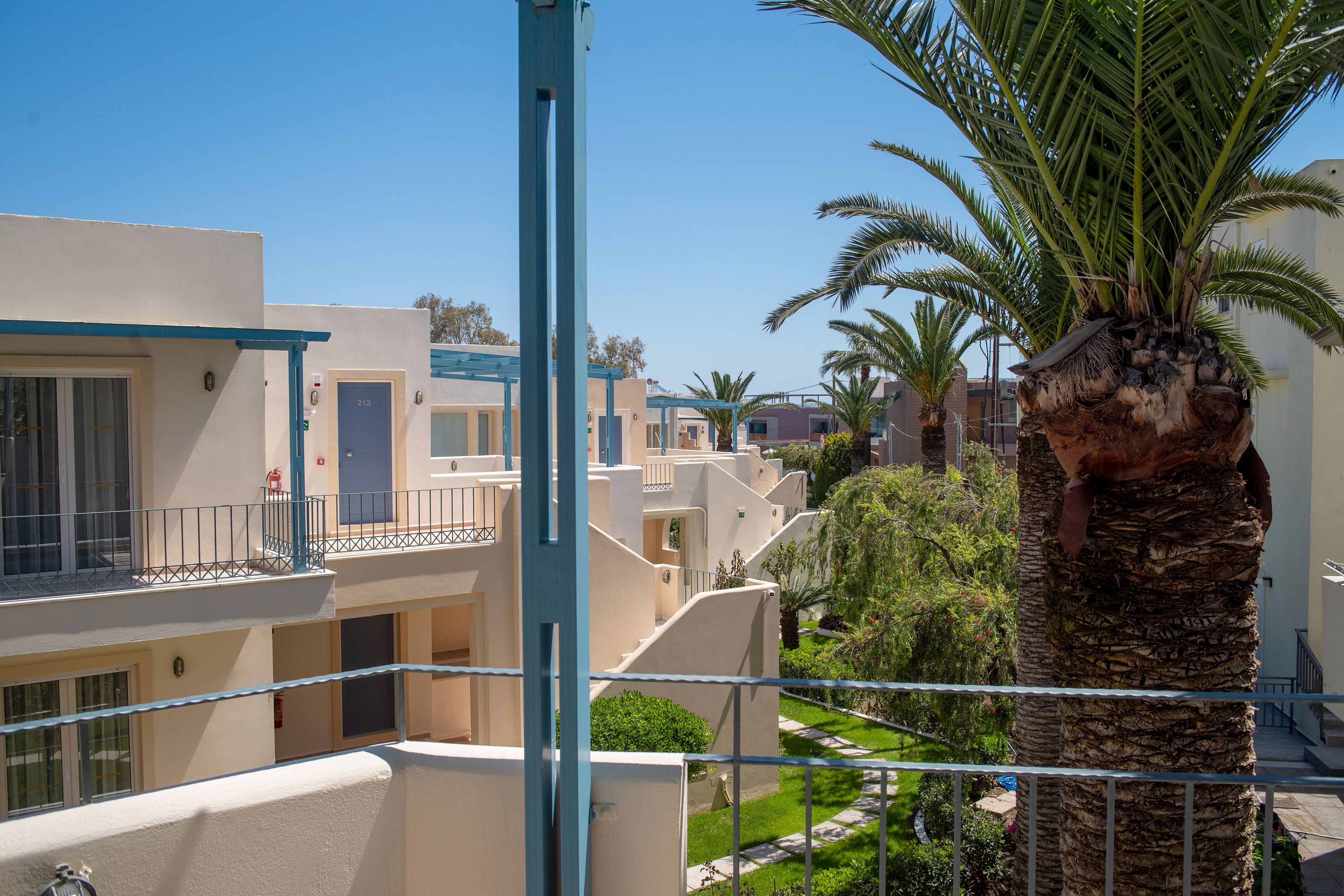 A multi-story residential building with balconies, a palm tree, and a clear sky.