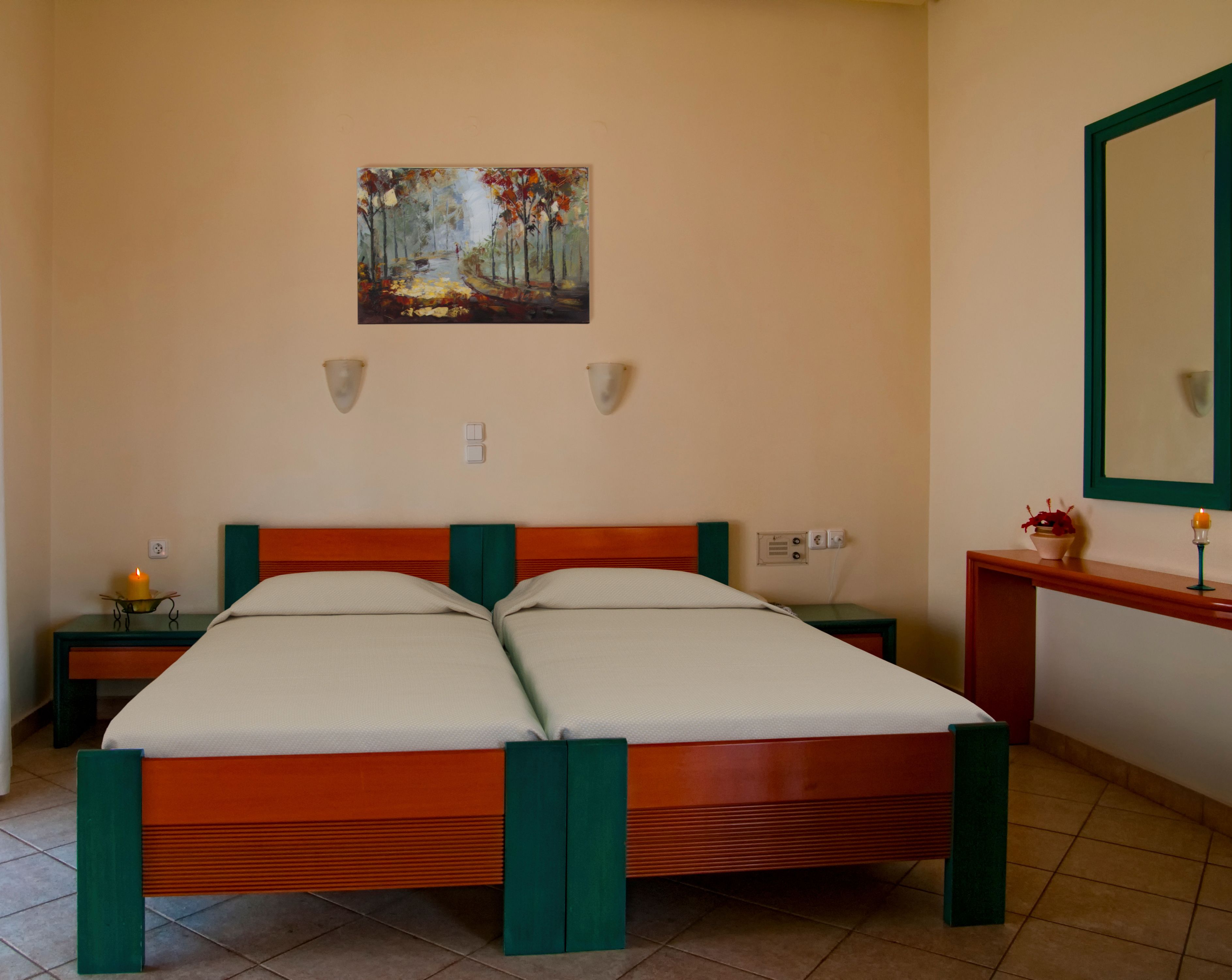 Una cama doble con estructura de madera y detalles verdes, un cuadro en la pared, una mesita de noche con una vela y un espejo en la pared.