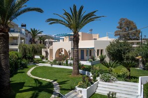 A residential area with a well-maintained lawn, palm trees, and a white staircase leading to a building entrance.