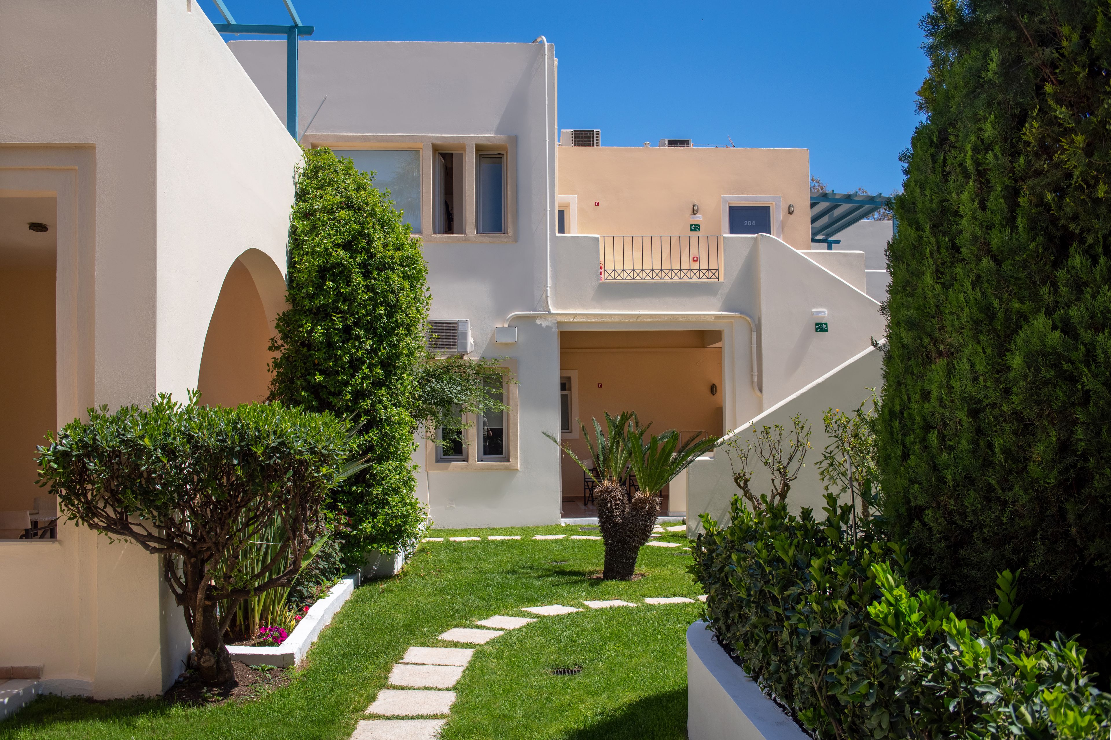 A modern building with a white facade, a central courtyard with a pathway, and a small tree.