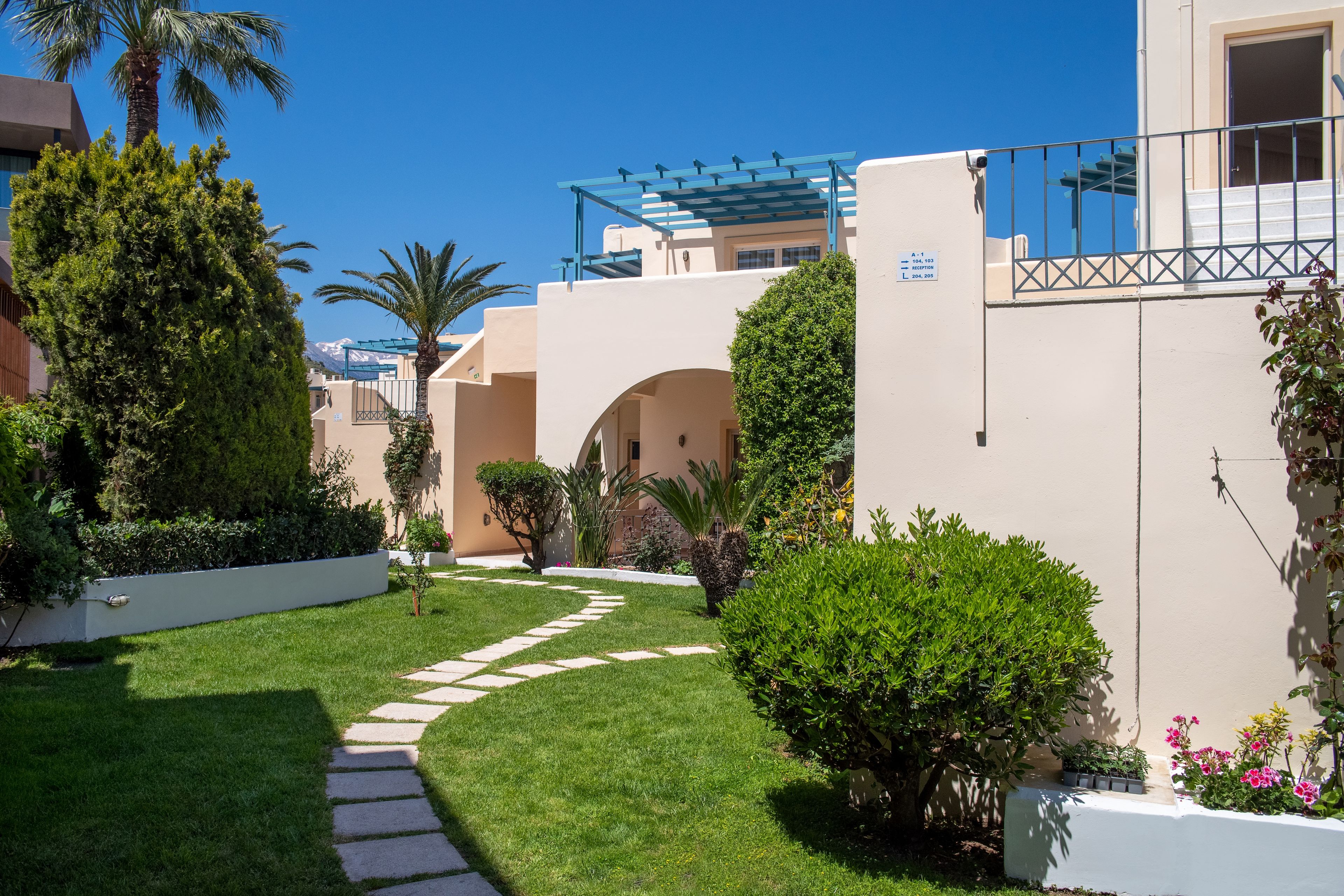 A well-maintained garden with a stone pathway leading to a building with a blue pergola.