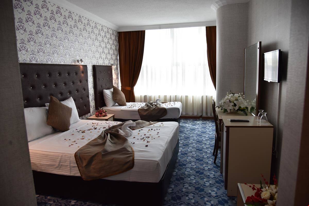 Habitación de hotel con dos camas, un escritorio, un televisor y un ventanal con cortinas.