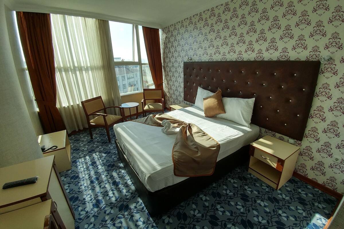 Una habitación de hotel con una cama grande, una silla, una mesita y una ventana con cortinas.