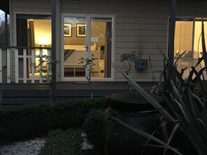 A house with a front porch, a small garden, and a visible interior with a bed and a chair.
