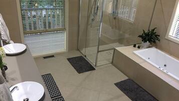 Ein modernes Badezimmer mit einer Duschkabine, zwei Waschbecken, einer Badewanne und einem Blumentopf.