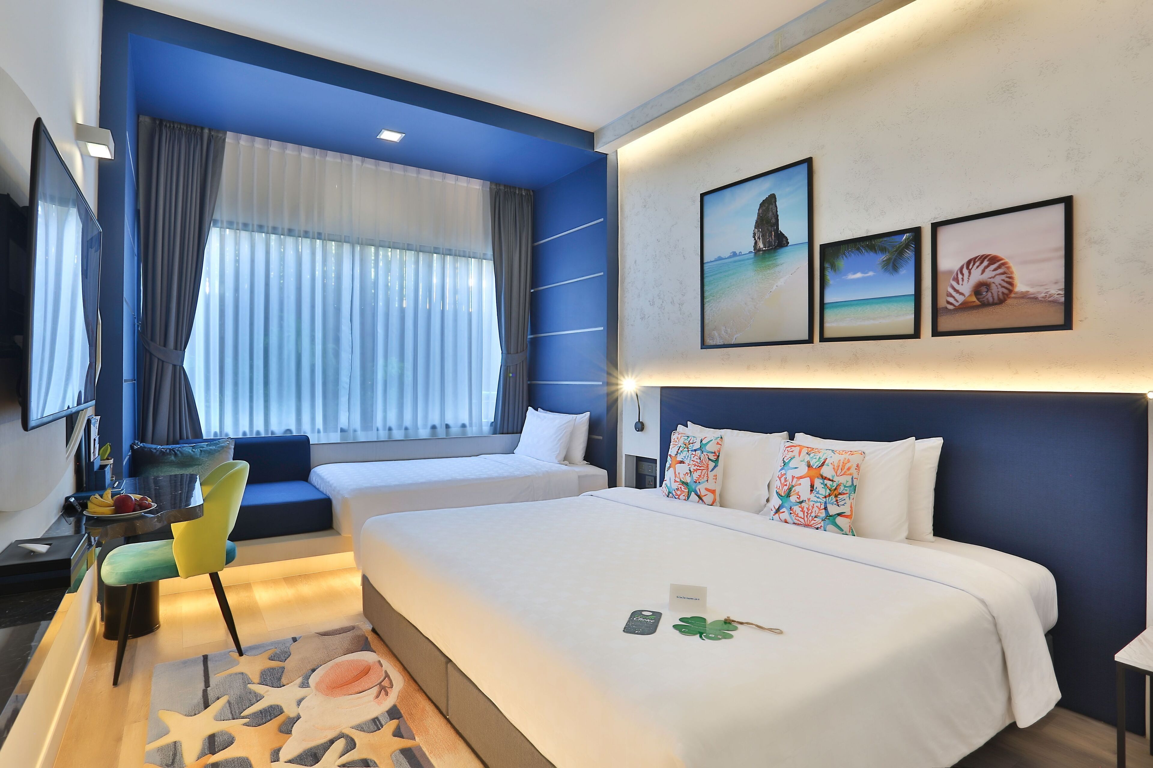 A hotel room with two beds, a desk with a chair, a TV, and artwork on the wall.