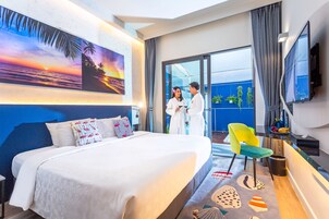 Habitación de hotel con una cama grande, televisor, balcón con vistas y un cuadro de un atardecer.