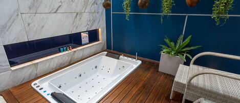 A modern bathroom with a freestanding bathtub, wooden flooring, and hanging plants.
