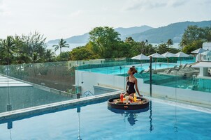 A poolside area with a glass barrier, lounge chairs, umbrellas, and a dining setup with food and drinks.