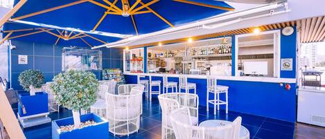 Un'area bar con mobili in vimini bianco, pareti blu e un soffitto con travi in legno.