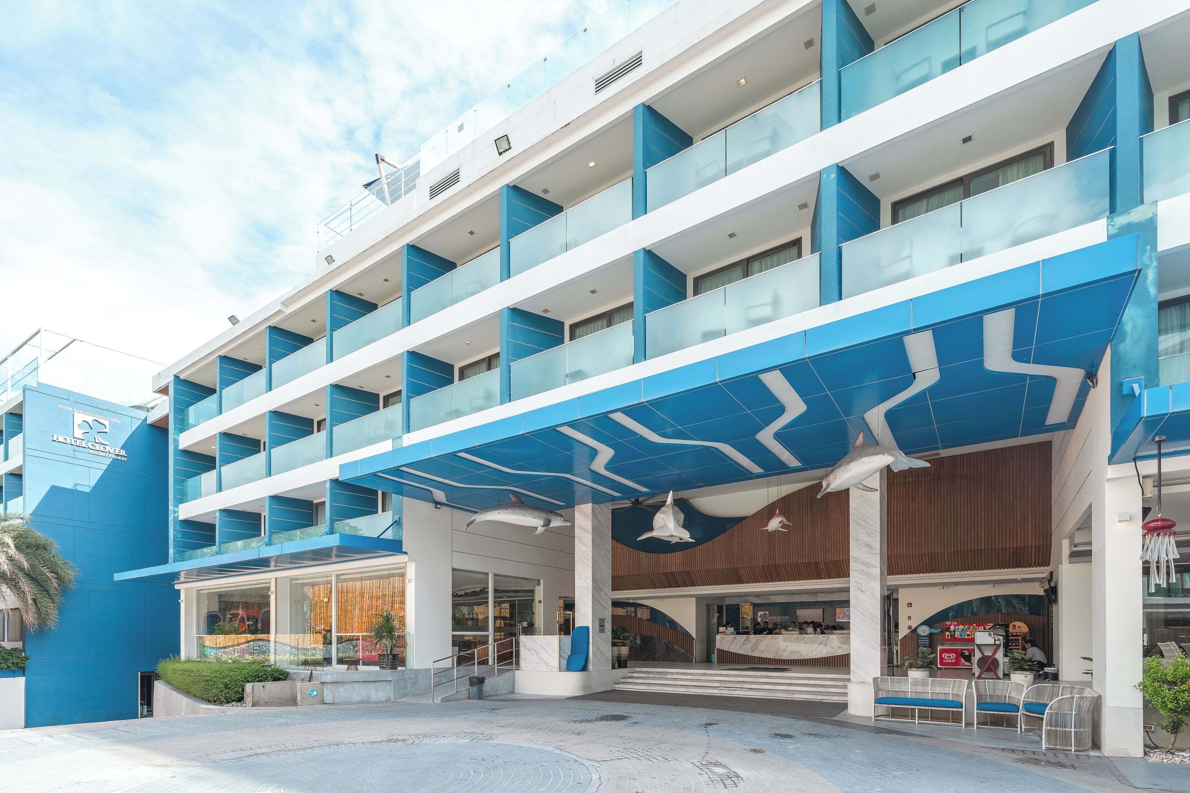 Ein mehrstöckiges Hotel mit blau-weißer Fassade, einem überdachten Eingangsbereich und einem sichtbaren Restaurant.