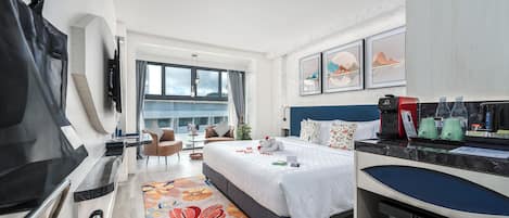 Una habitación de hotel moderna con una cama, un escritorio con cafetera, un refrigerador y vistas a la ciudad.
