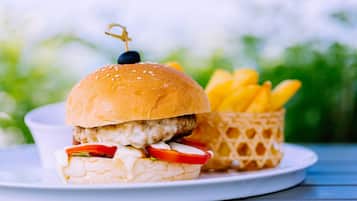 A burger with a sesame seed bun, a chicken patty, lettuce, tomato, and a blue cheese slice, accompanied by a side of fries in a waffle container.