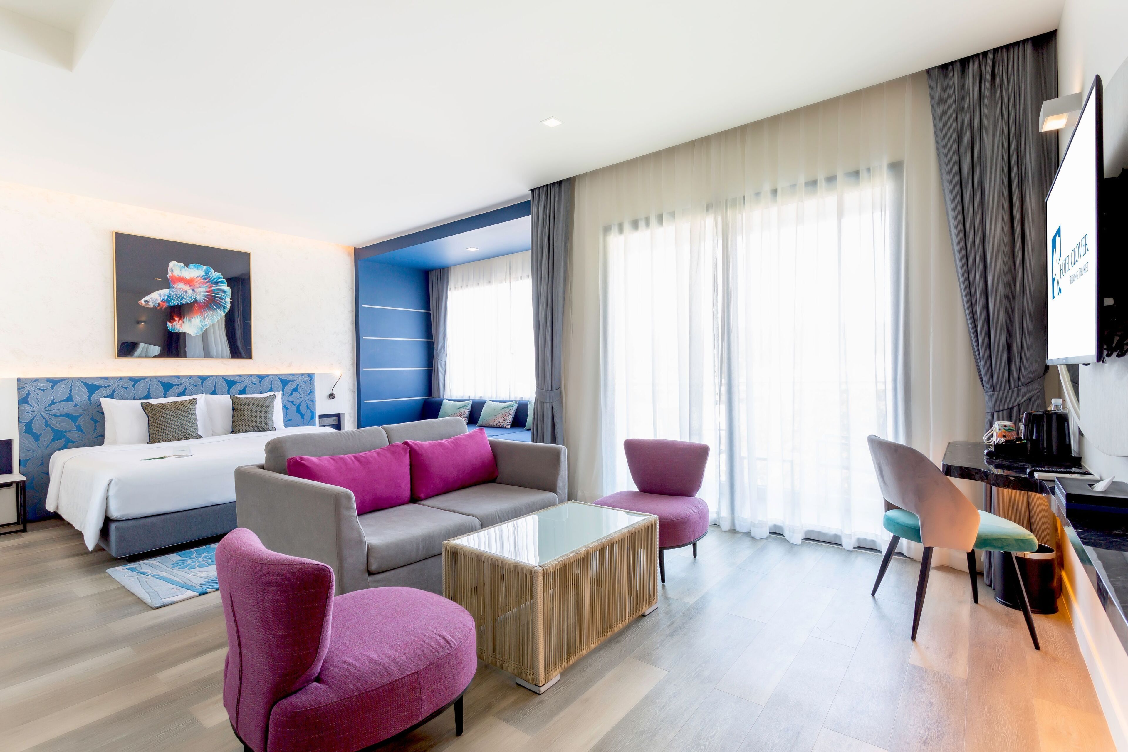 Ein modernes Hotelzimmer mit Bett, Sofa, zwei Sesseln, einem Couchtisch und einem Fernseher.