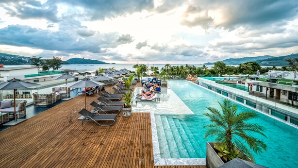 A rooftop pool area with lounge chairs, umbrellas, and a view of the sea and mountains. - Hotel Clover Patong Phuket (Patong)
