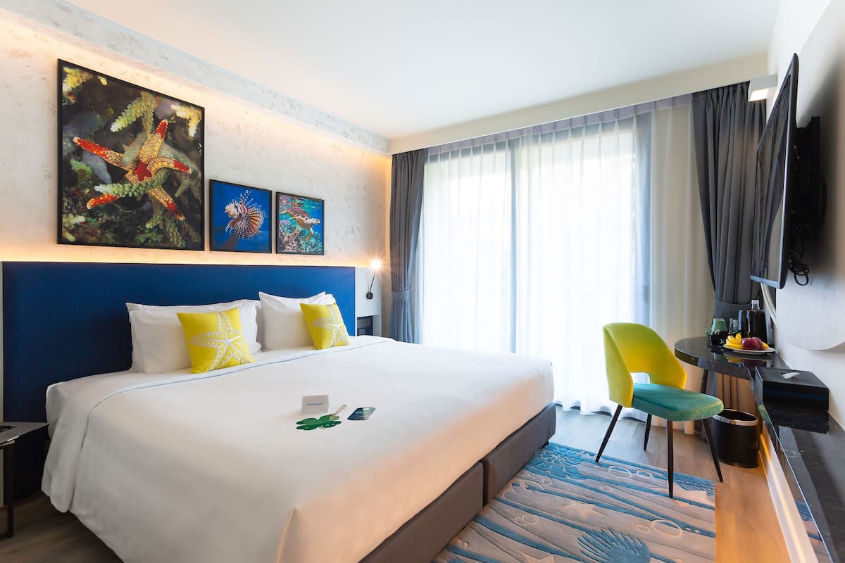 Habitación de hotel con una cama grande, un escritorio, una silla y obras de arte en la pared.