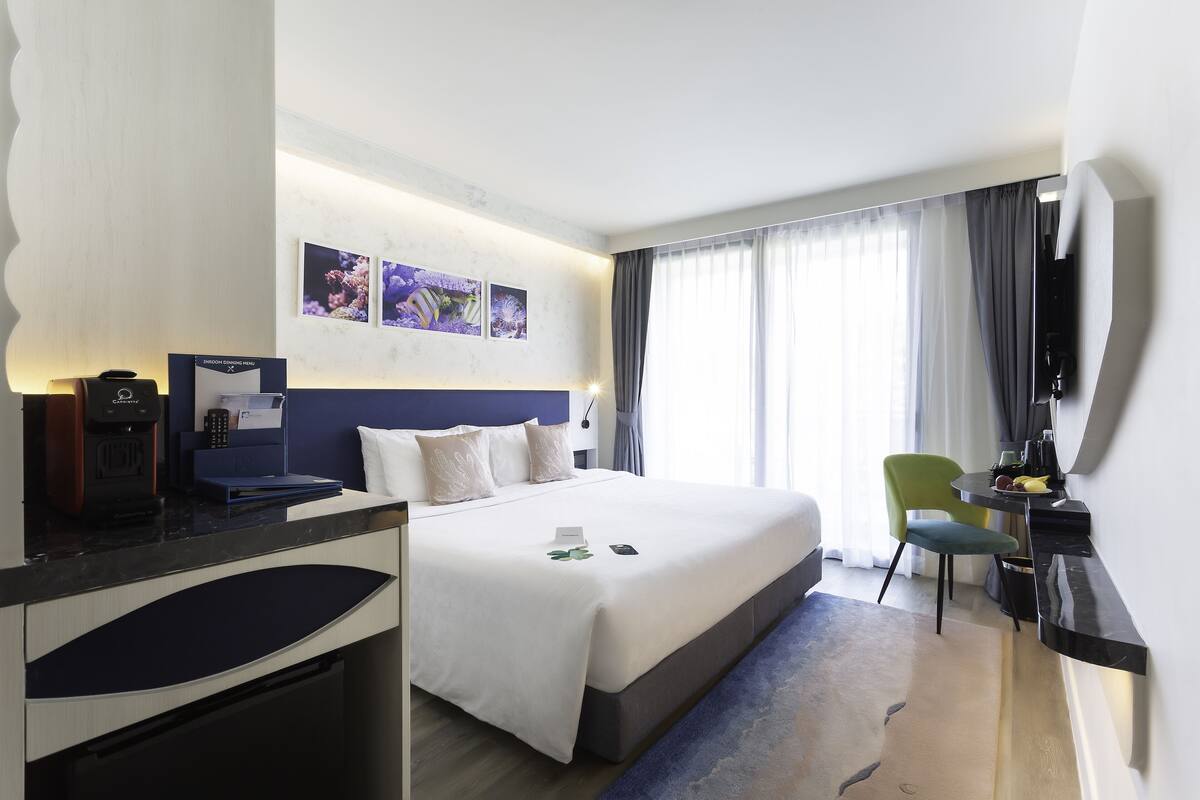 Una habitación de hotel con cama, escritorio, silla, cafetera y televisión.