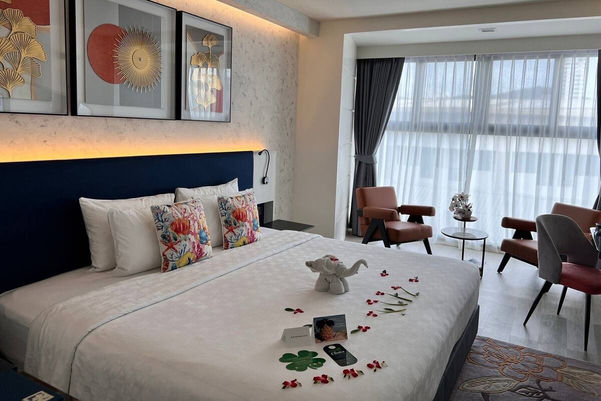 Una habitación de hotel con una cama grande, cabecera, escritorio, dos sillas y una ventana con cortinas.