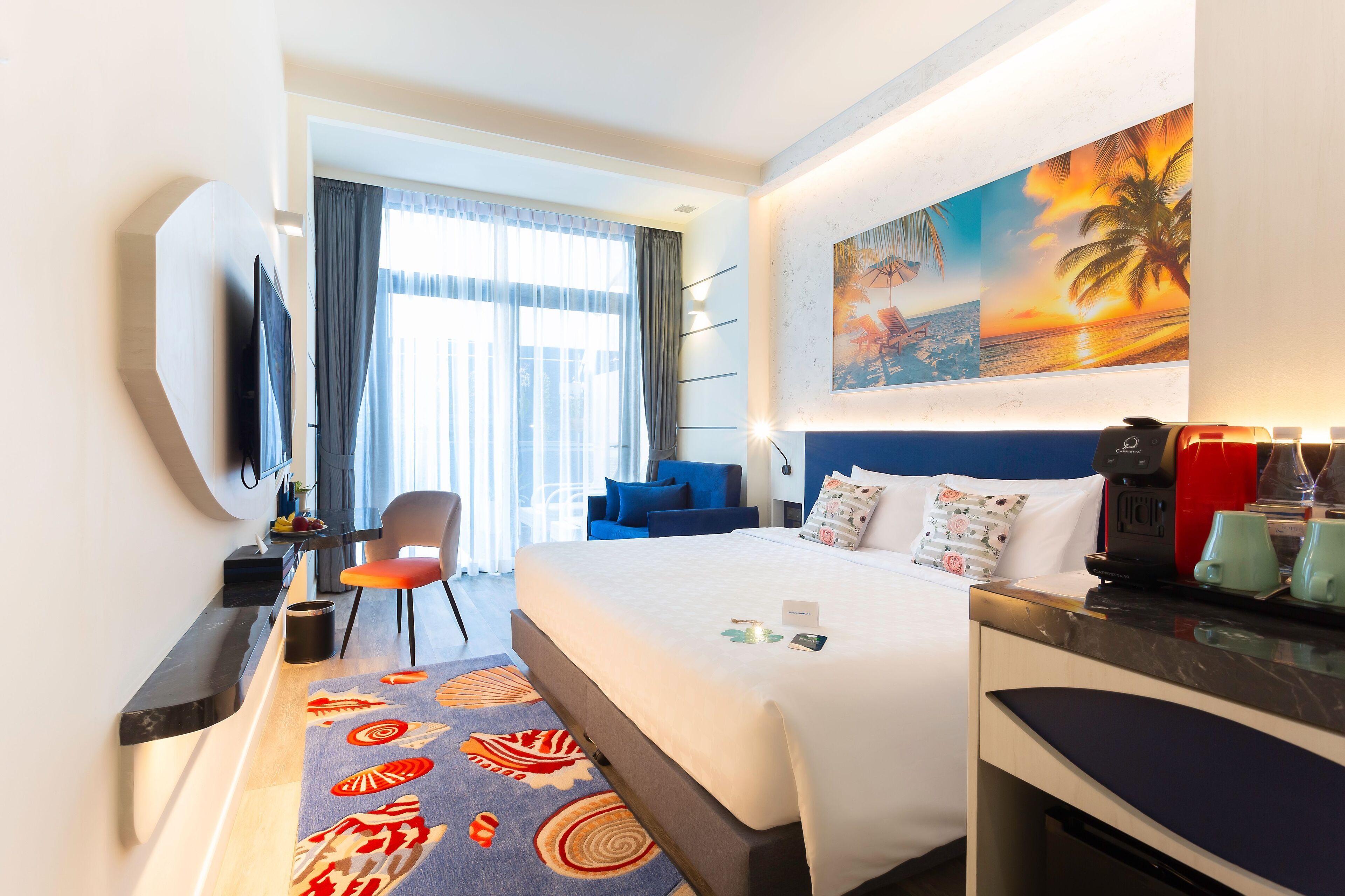 A hotel room with a bed, a desk, a chair, a TV, a painting, and a coffee machine.