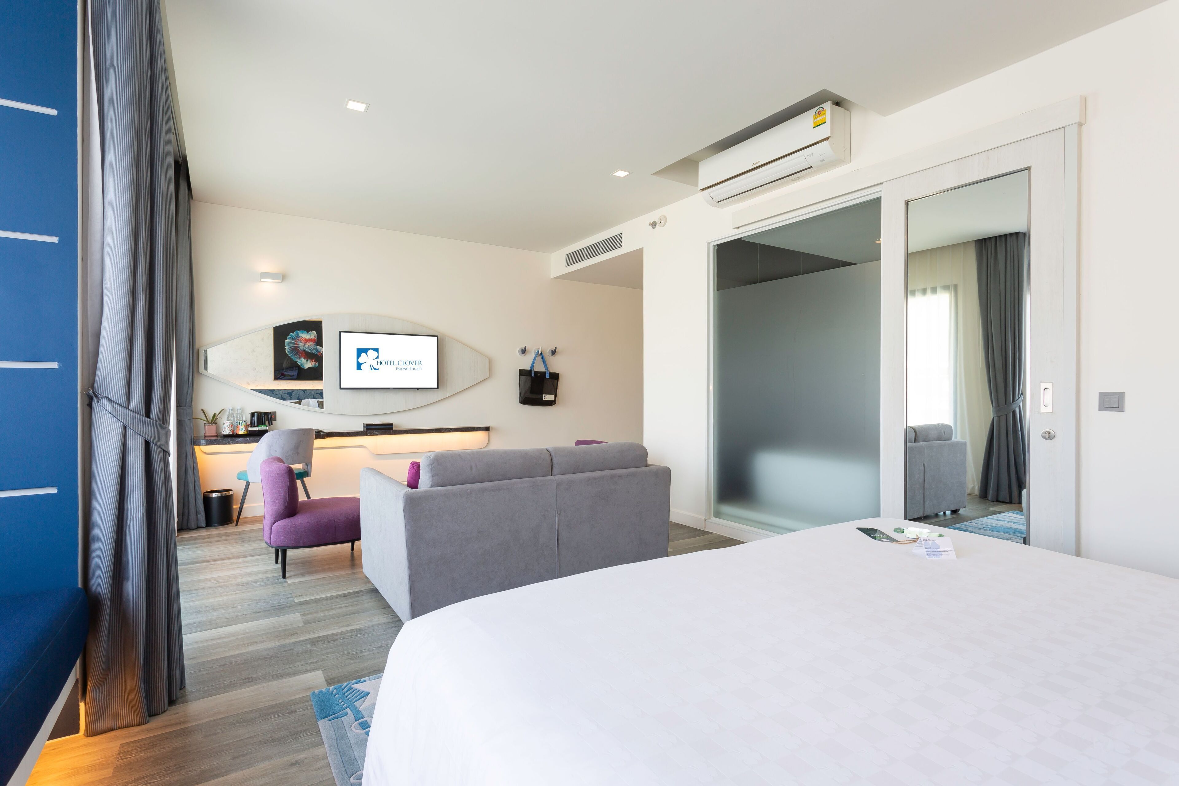 A modern hotel room with a large bed, a sofa, a desk with a computer, and a TV.