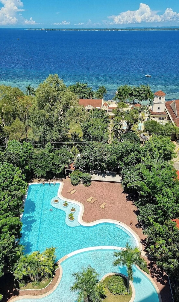 A resort with a large swimming pool, lush greenery, and a view of the ocean. - La Mirada Residences (Lapu-Lapu)