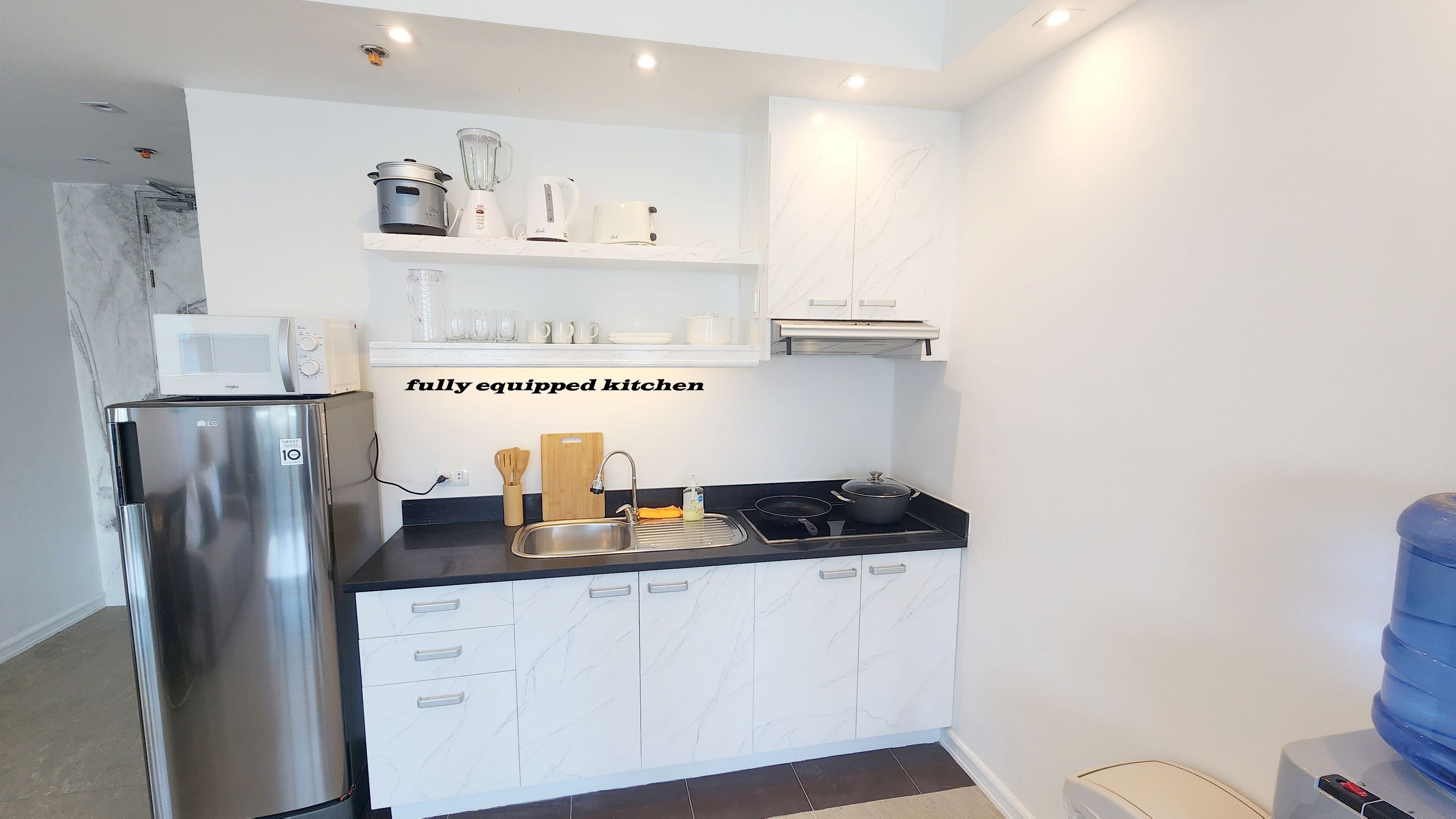 A compact kitchen with a stainless steel refrigerator, a black countertop, and white cabinets with marble-like patterns.
