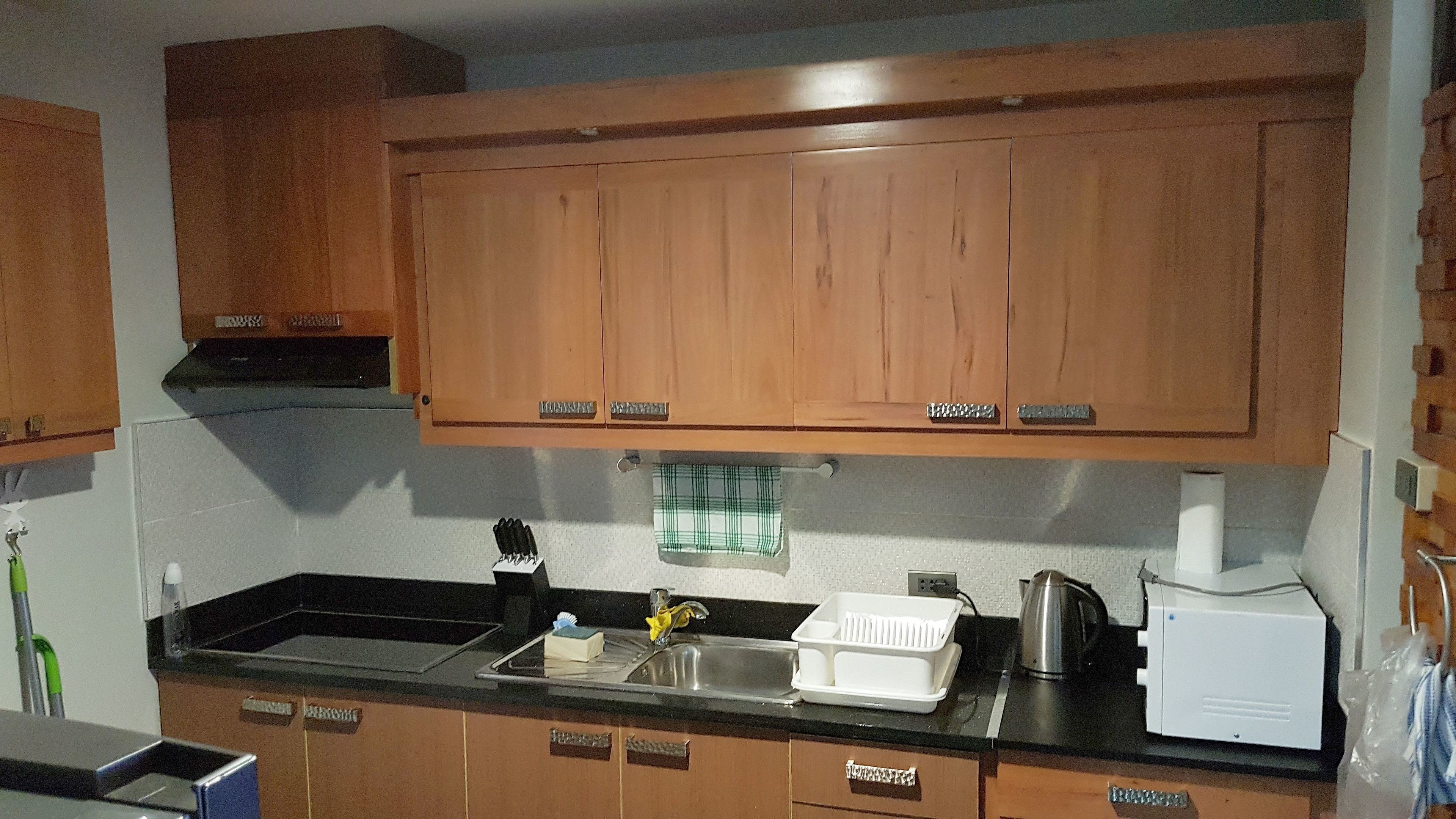 Une cuisine avec des meubles en bois, un plan de travail noir, un évier, une bouilloire et un appareil électroménager blanc.