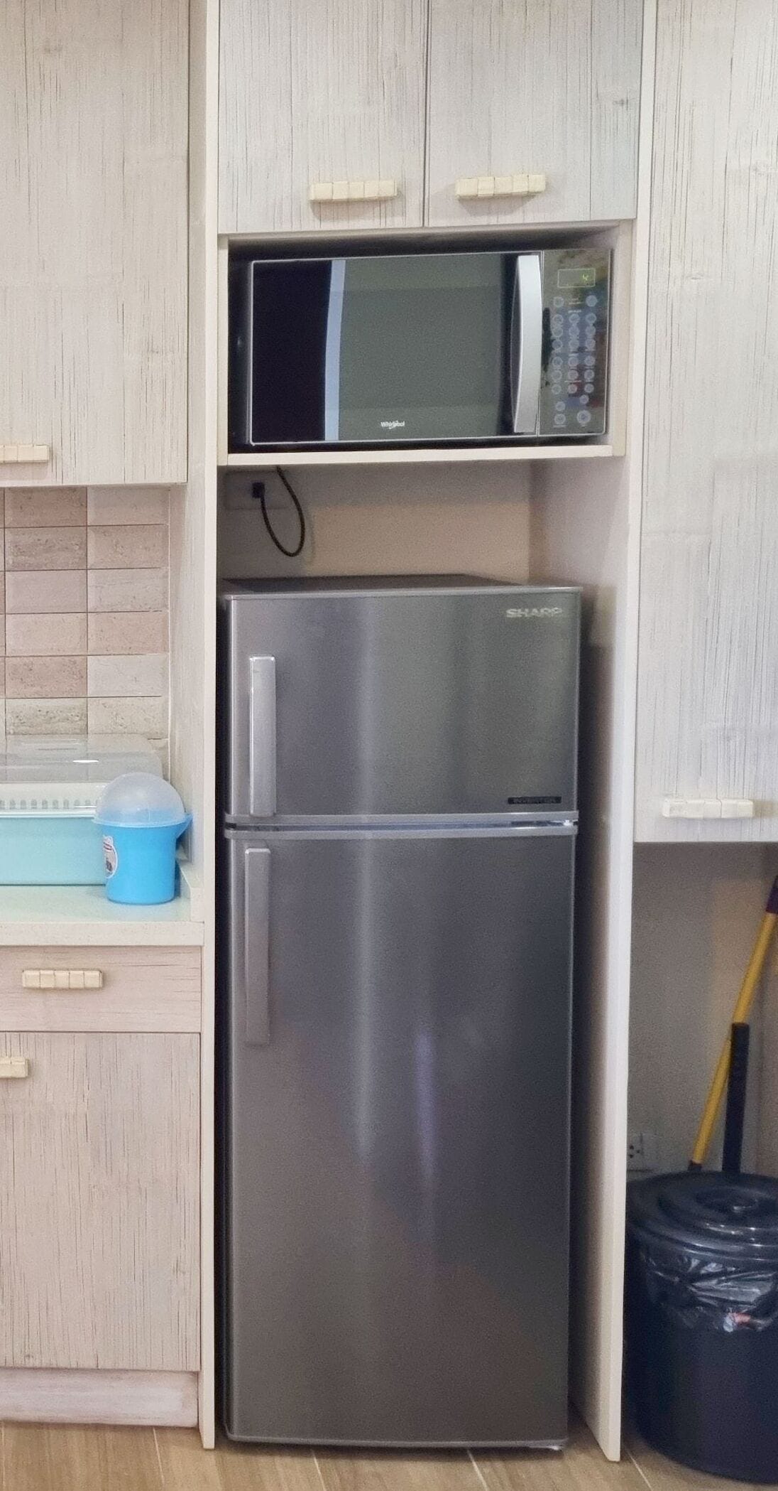 Eine kleine Küche mit einem Edelstahl-Kühlschrank, einer Mikrowelle und einer blauen Aufbewahrungsbox.