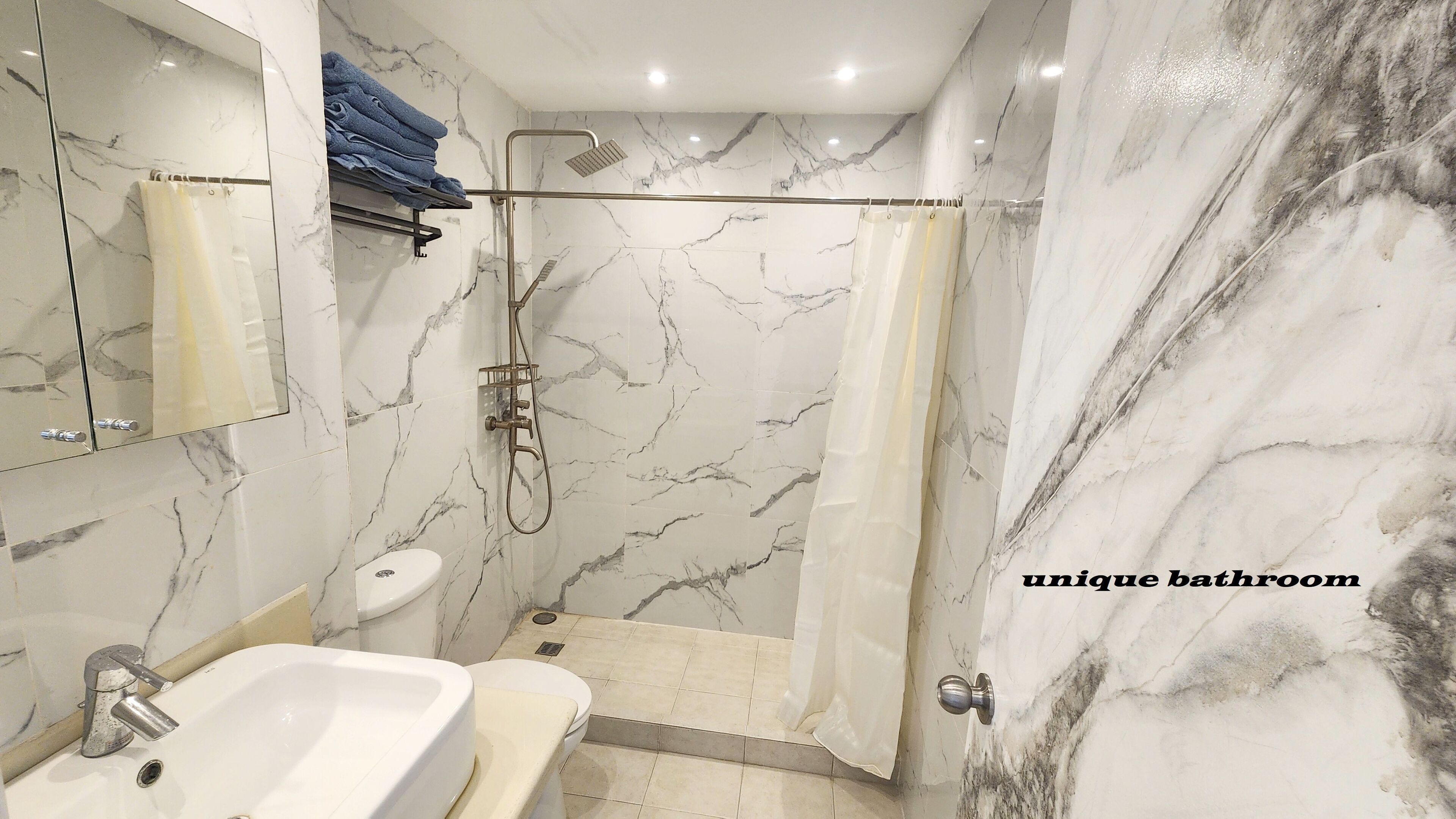 Een badkamer met een marmeren wand, een wastafel, toilet en een douchehoek.