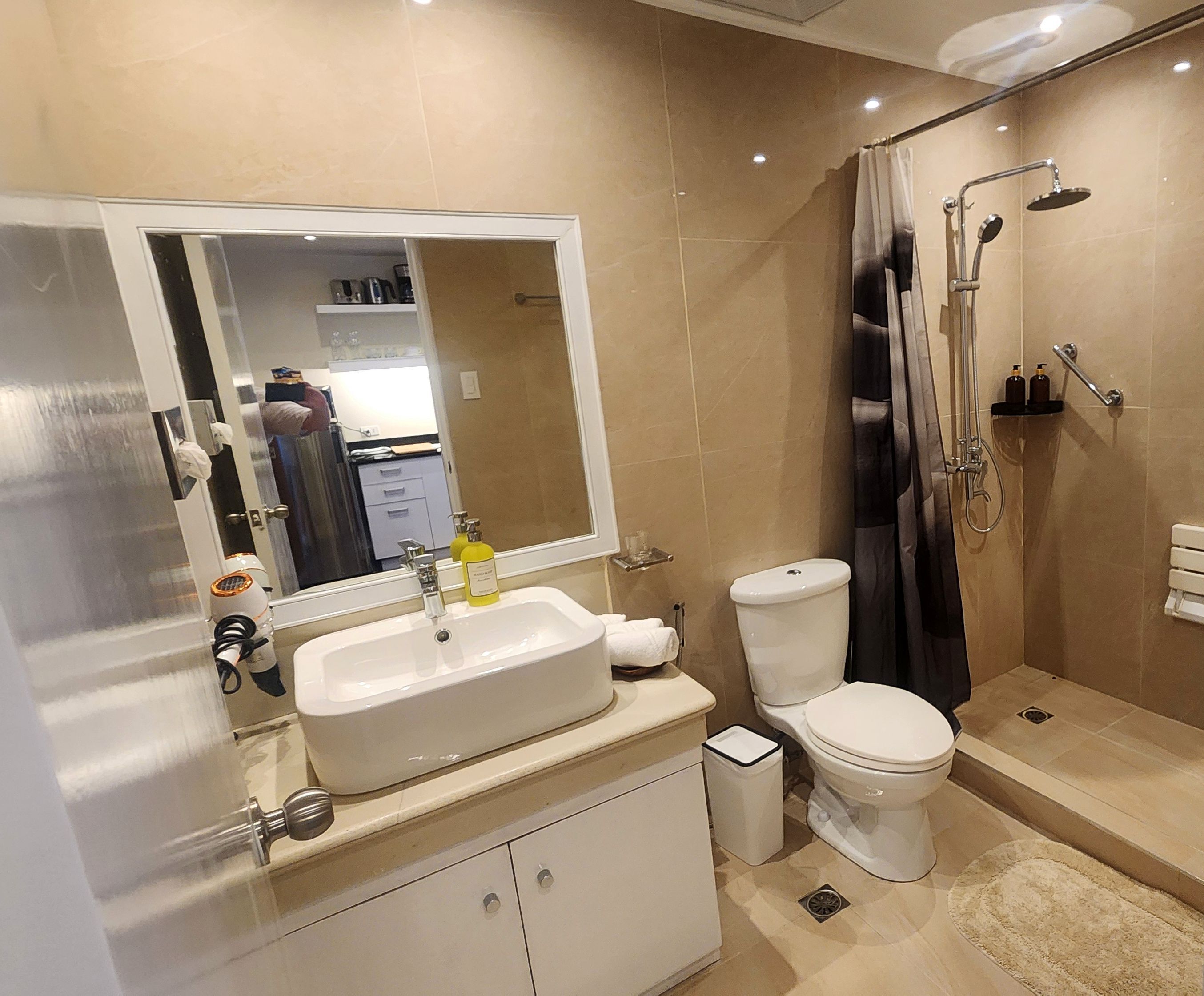 Un baño moderno con un espejo grande, un lavamanos, un inodoro y una zona de ducha.