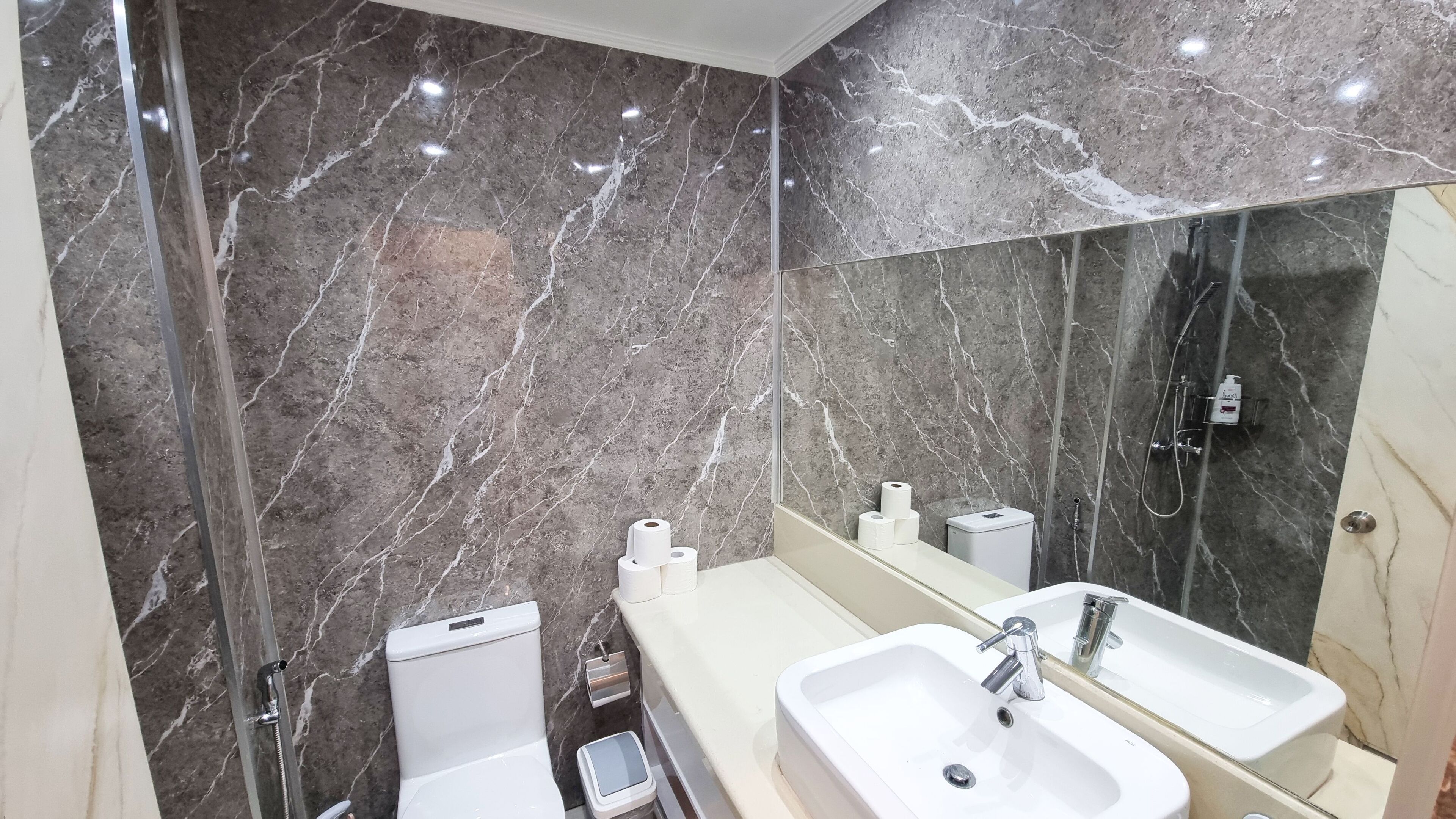 A modern bathroom with marble walls, a large mirror, a sink, and a toilet.