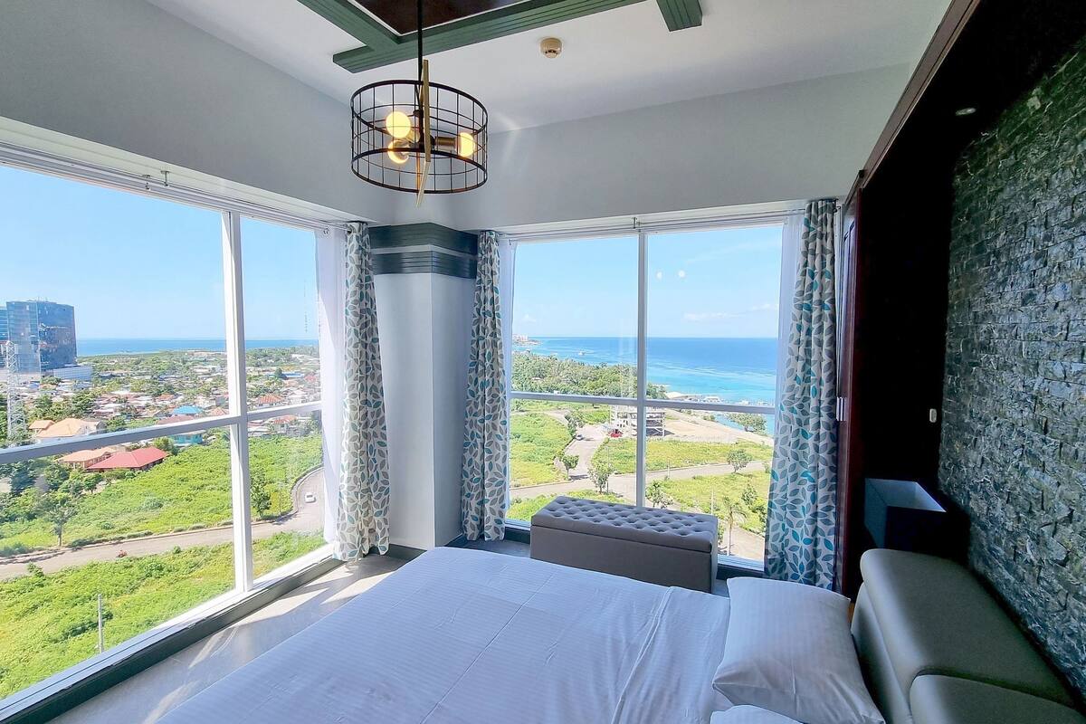A bedroom with a large window offering a view of the city and ocean.