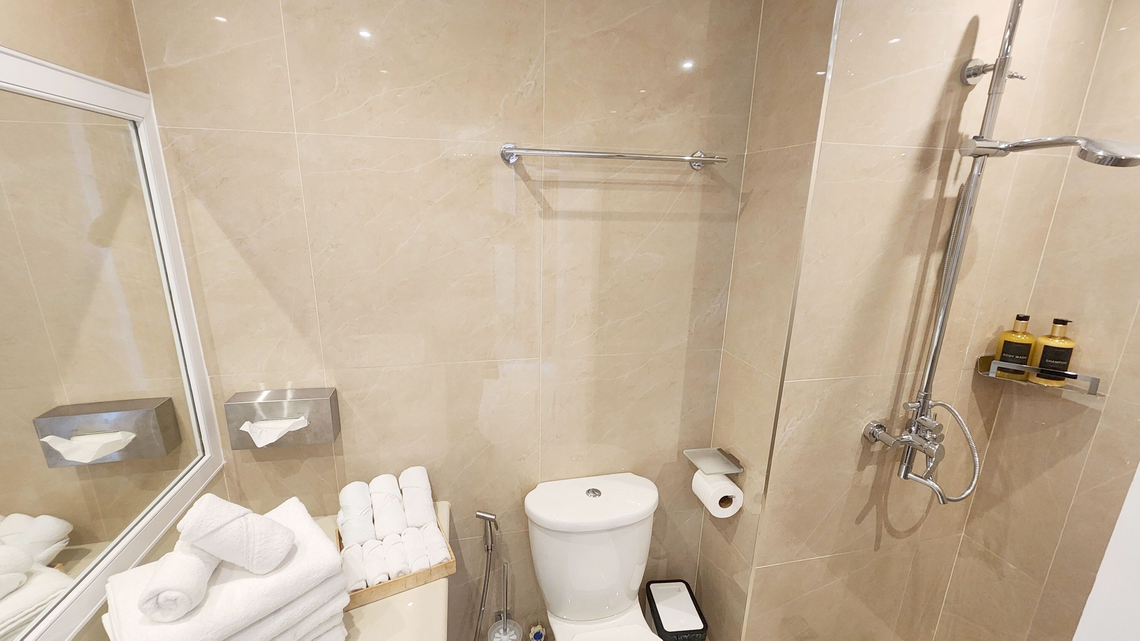 Moderni kylpyhuone, jossa on wc, bidee ja suihku. Pyyhkeet ja hygieniatuotteet ovat seinällä.